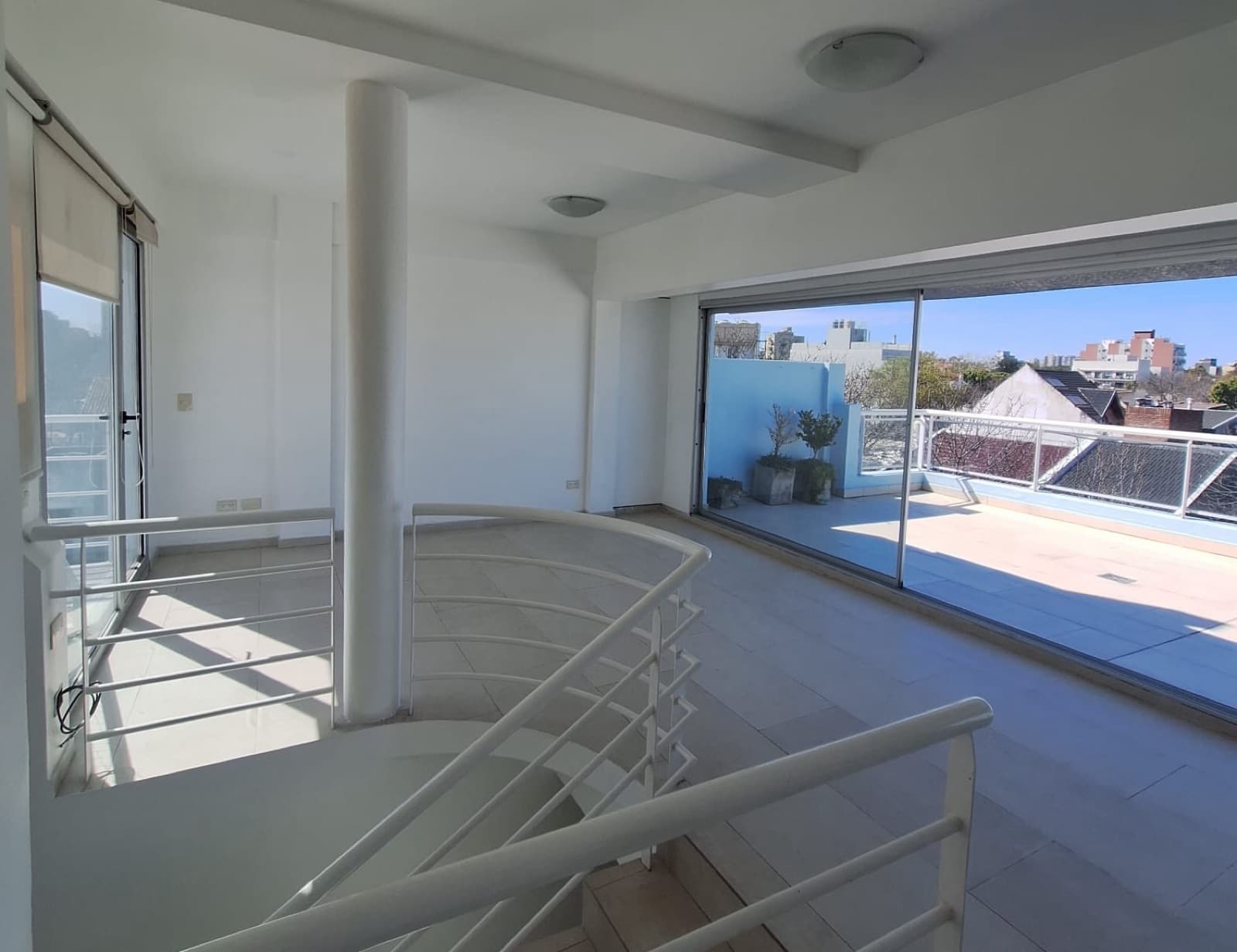 Living con escalera caracol, columna y amplios ventanales al exterior.