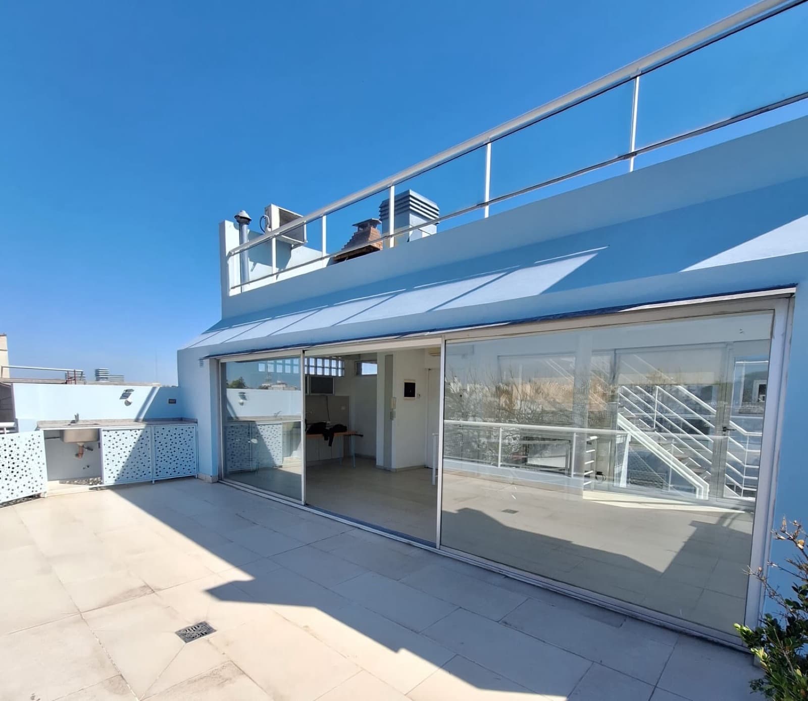 Balcón terraza con mesada exterior y puertas de vidrio al interior.