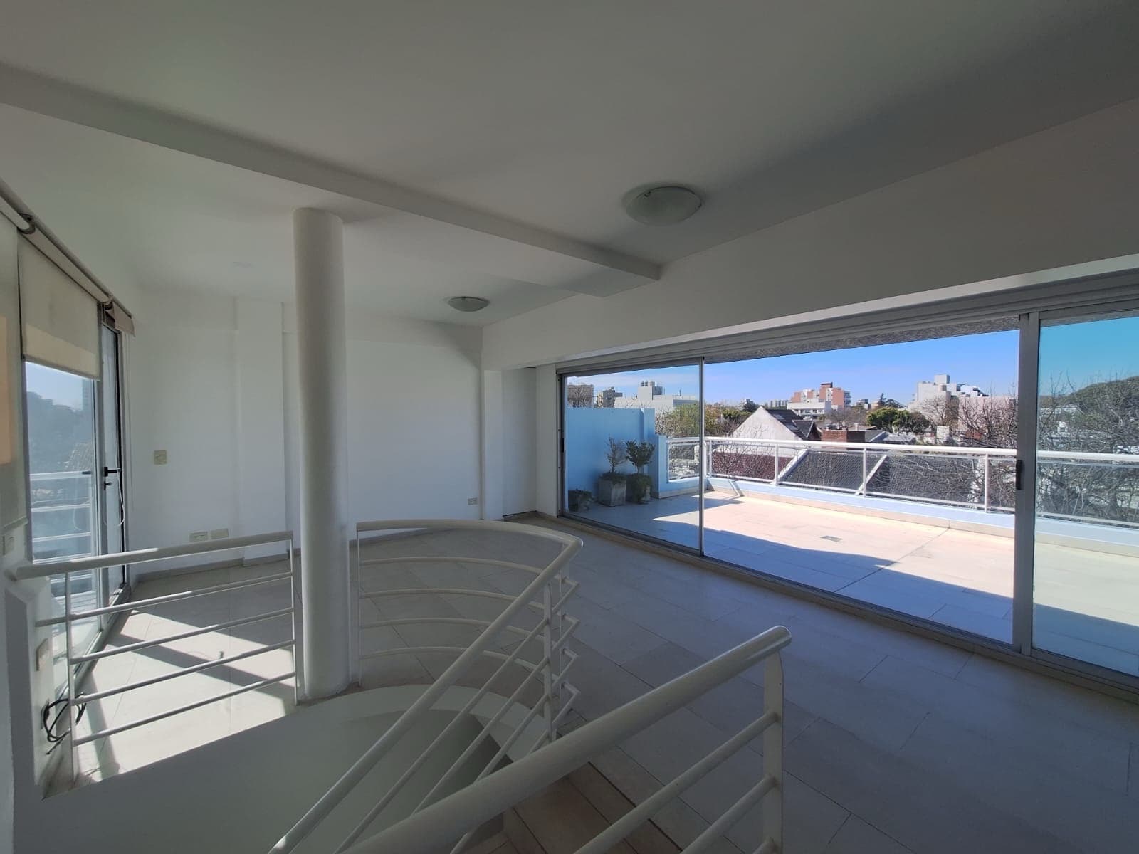 Living-comedor con escalera caracol y ventanal con vista exterior.