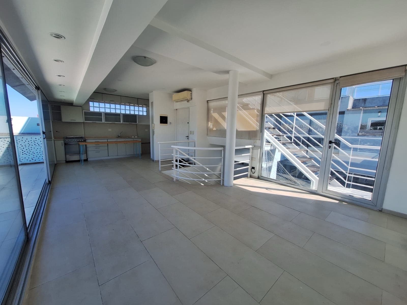 Living-comedor con cocina integrada y grandes ventanales.