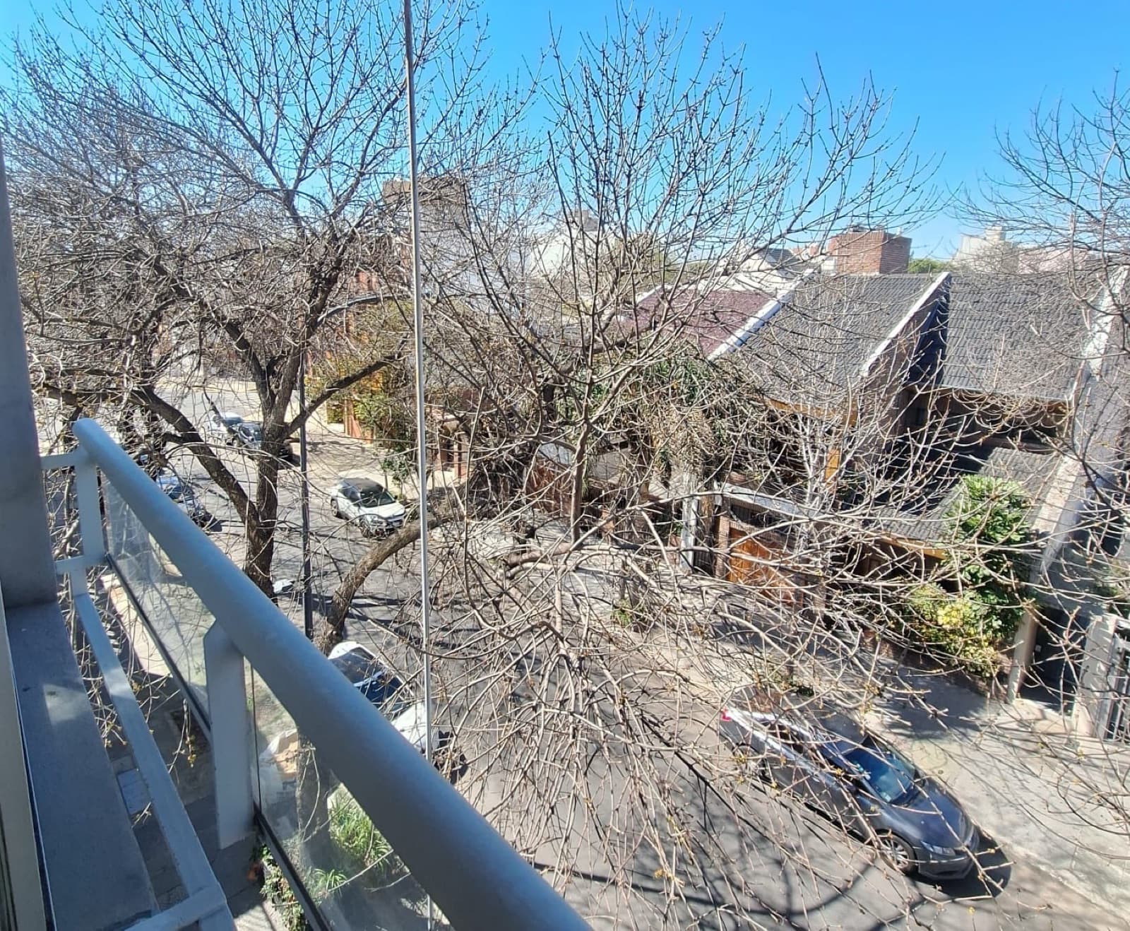 Vista desde balcón a calle con árboles y edificios.