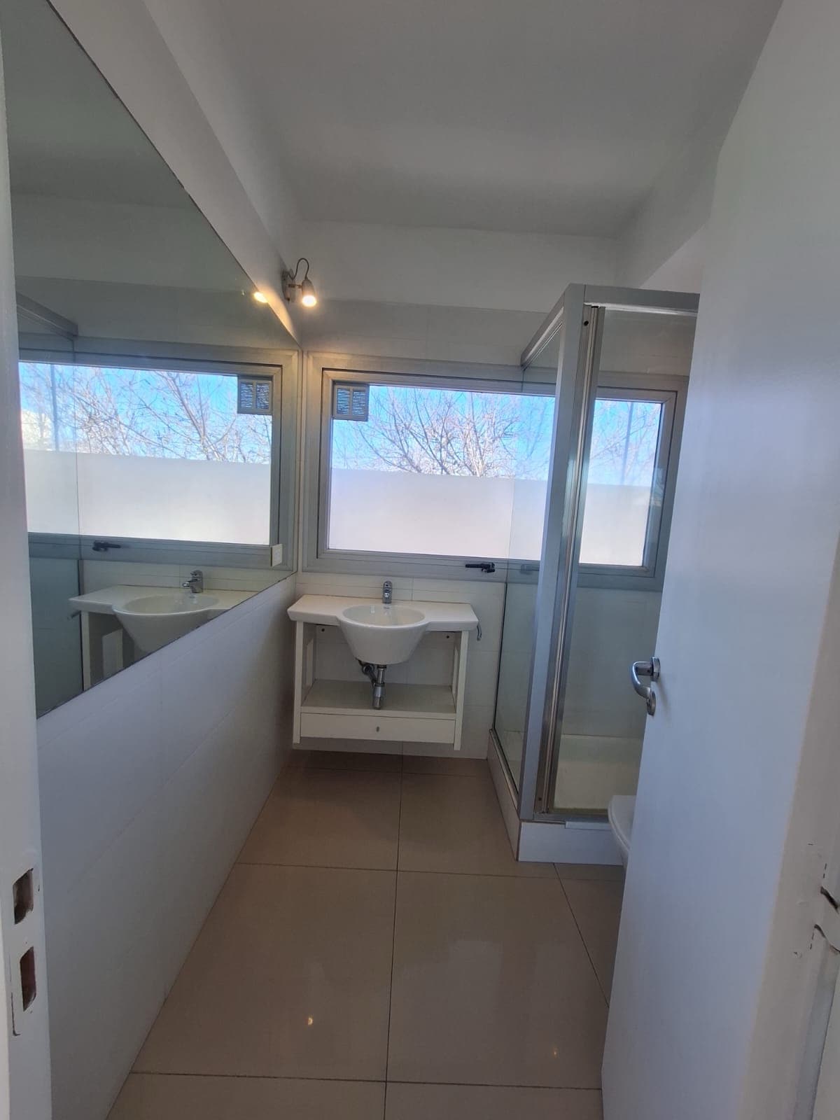 Baño completo con ducha, lavatorio y espejo grande.