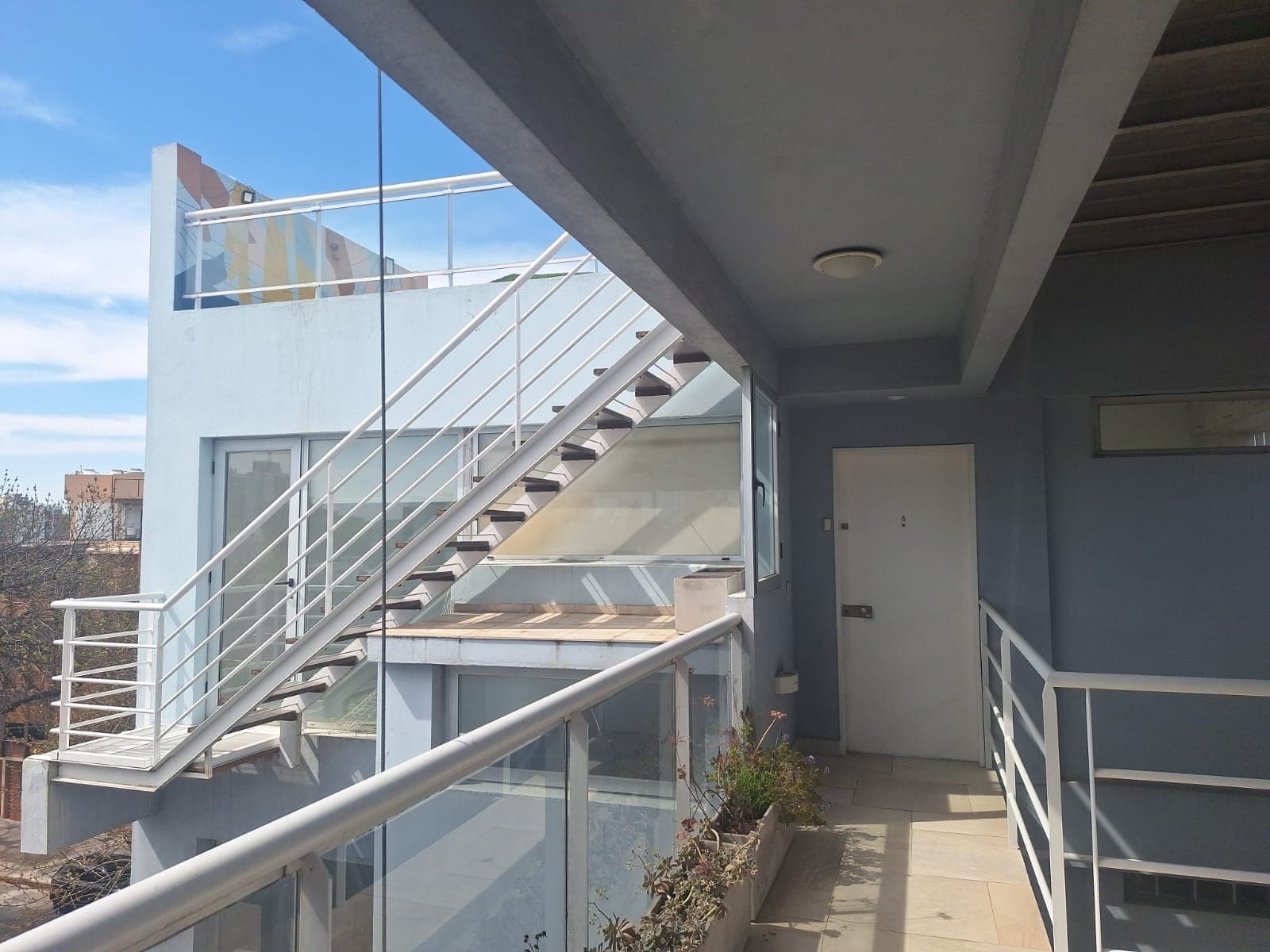 Pasillo exterior del edificio con escalera y barandas blancas.