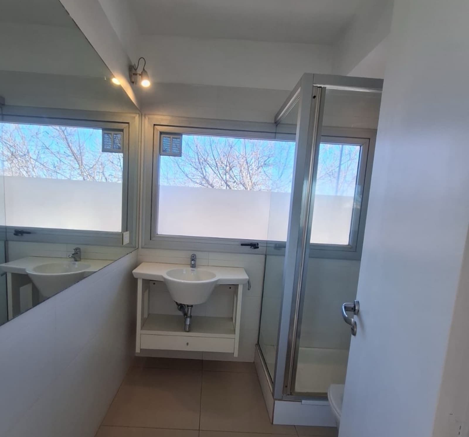 Baño con lavatorio, mueble, espejo y mampara de ducha.