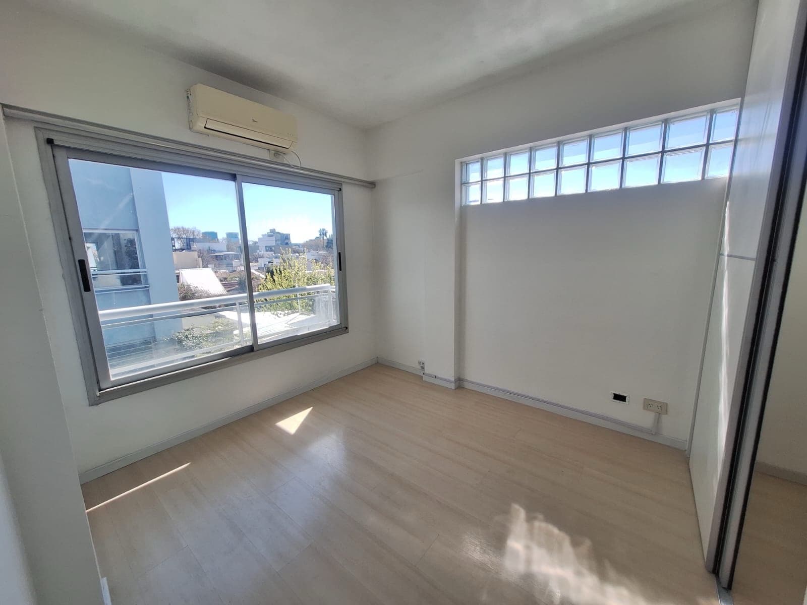 Dormitorio con ventanal, bloques de vidrio y aire acondicionado.