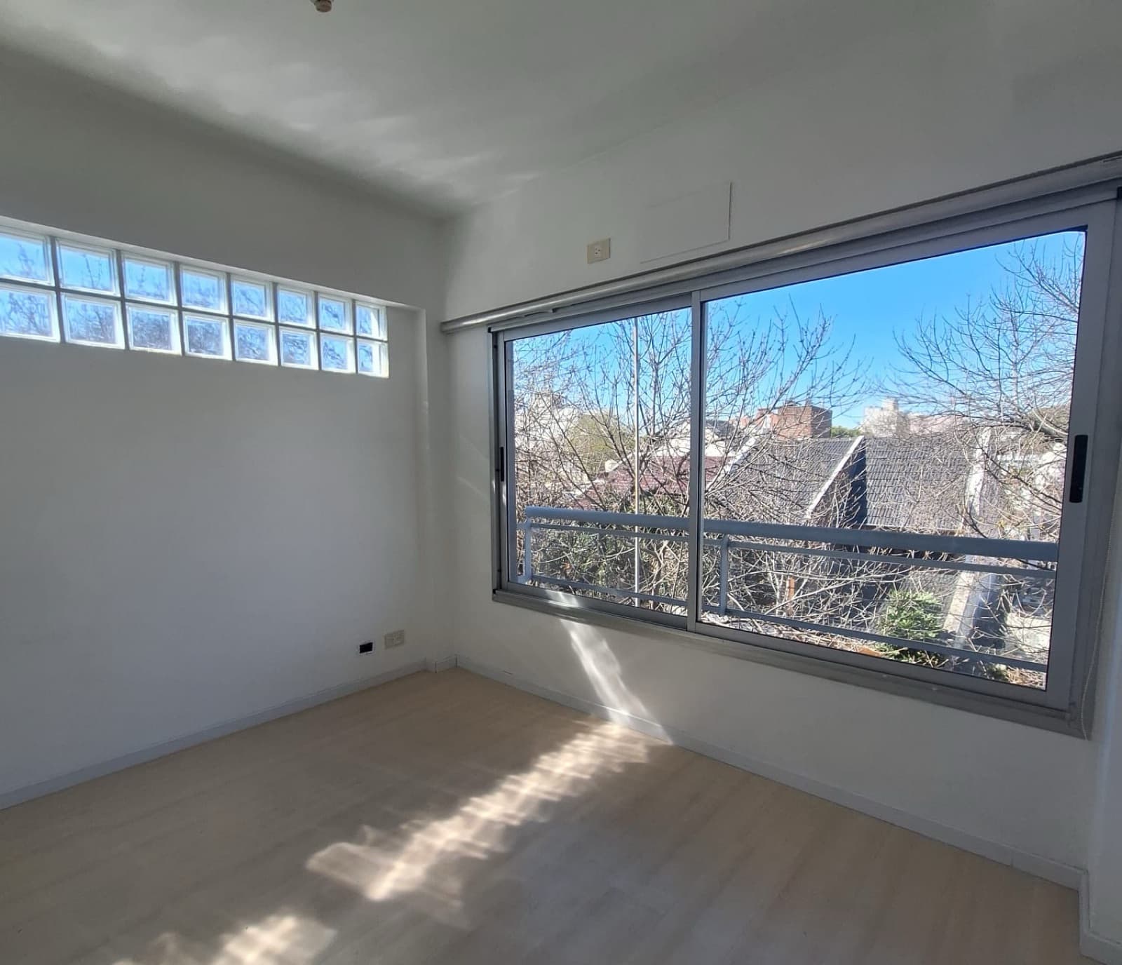 Dormitorio vacío con ventana y bloques de vidrio en pared.