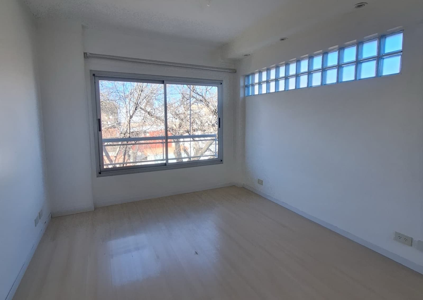 Dormitorio con amplia ventana, bloques de vidrio y piso de madera.
