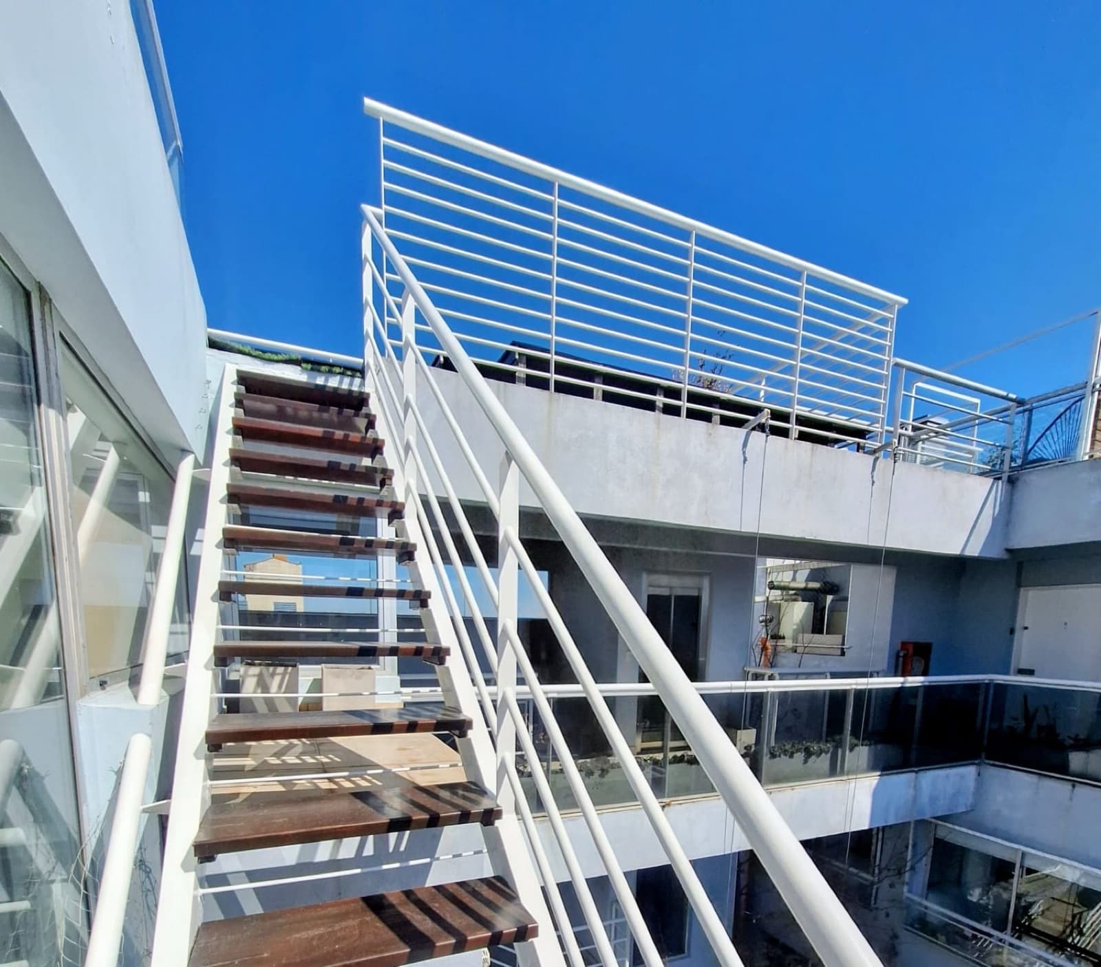 Escalera exterior blanca que conecta con la terraza superior.