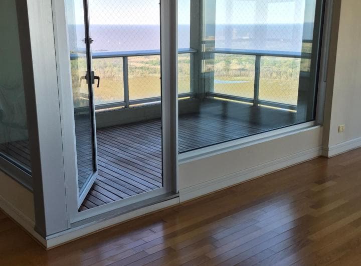 Balcón con deck de madera y baranda de vidrio, acceso desde el interior.