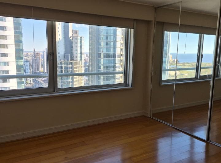 Dormitorio vacío con placard espejado y ventana con vista a edificios.