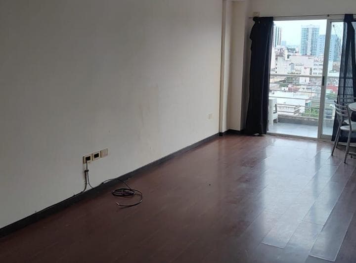 Living vacío con piso de madera y salida a balcón con vista a la ciudad.