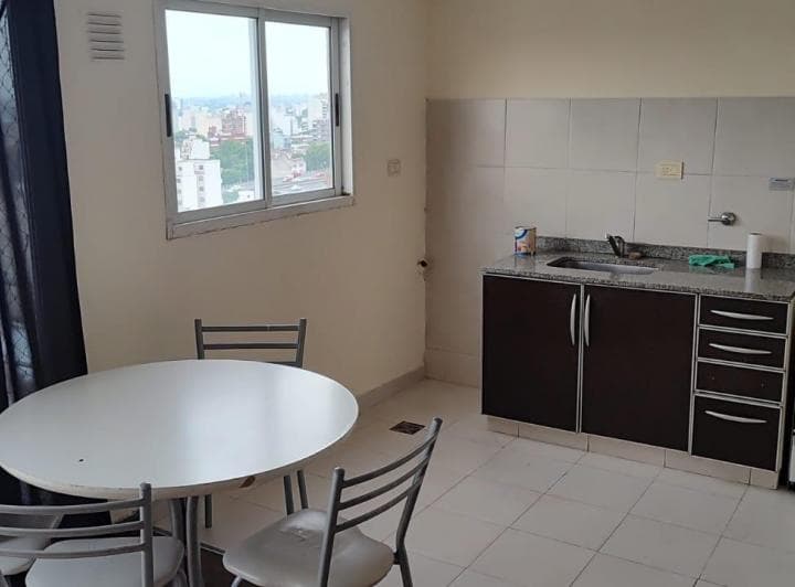 Cocina integrada con mesada, mesa redonda con sillas y ventana a la ciudad.