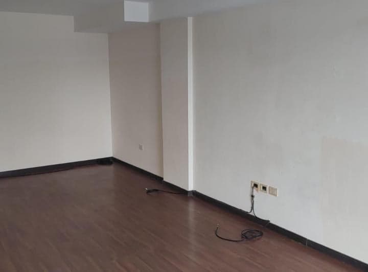 Living vacío con piso de madera y paredes blancas, desde otro ángulo.