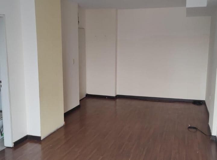 Living vacío con piso de madera y paredes claras, vista hacia la puerta.