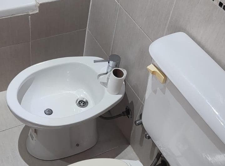 Toilette con bidet e inodoro, azulejos claros en la pared.
