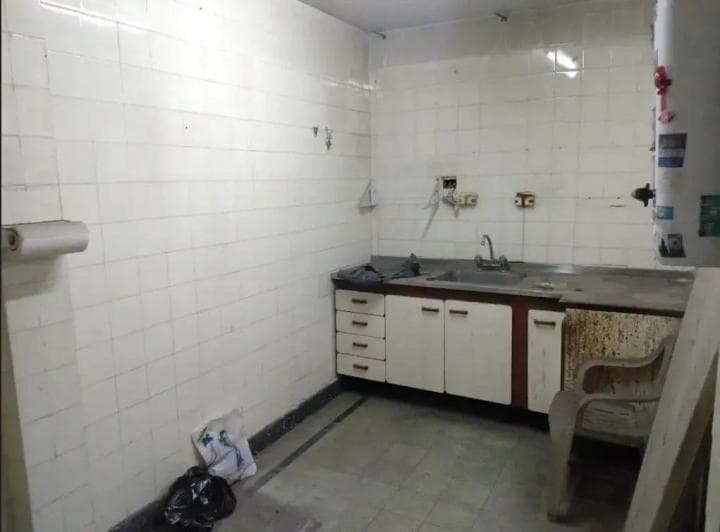 Cocina con mesada, bacha, alacenas viejas y paredes con azulejos blancos.