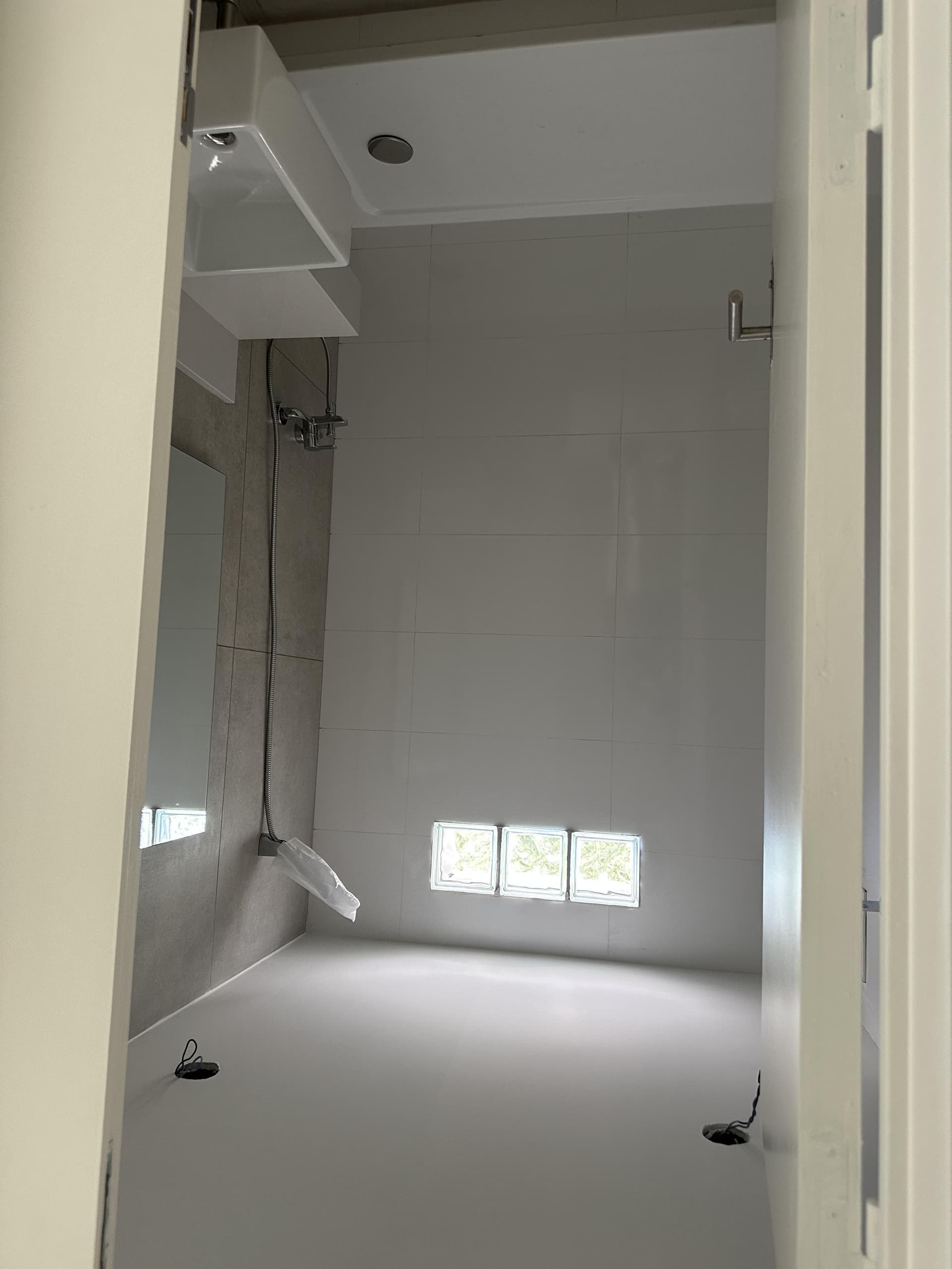 Baño con ducha, lavatorio, grifería en pared y azulejos claros.