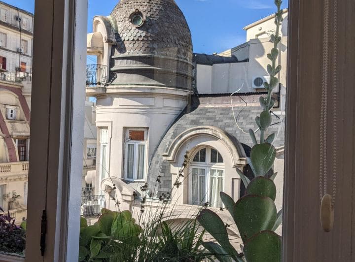 Vista desde la ventana con edificios, una cúpula antigua y plantas.