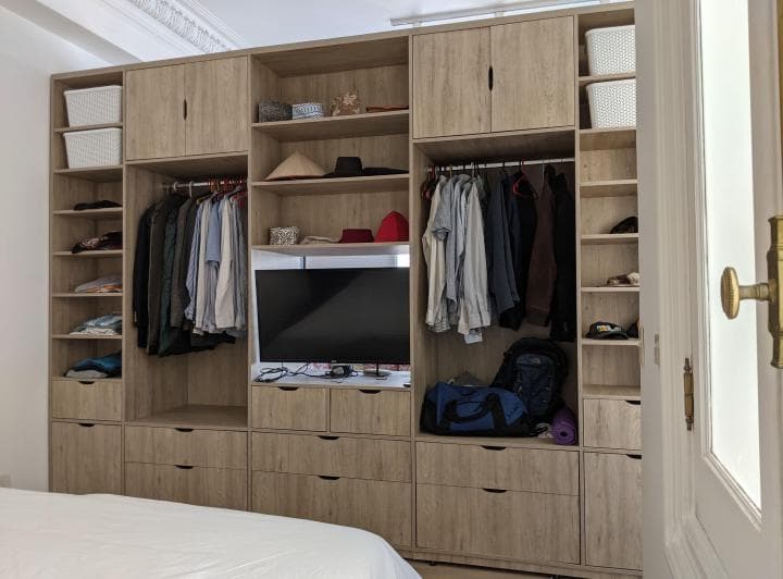 Dormitorio con amplio placard de madera, ropa colgada y estantes.