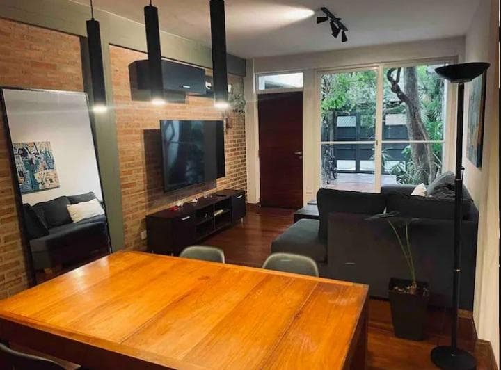 Living comedor con sofá, televisión, mesa de madera y vista al patio.