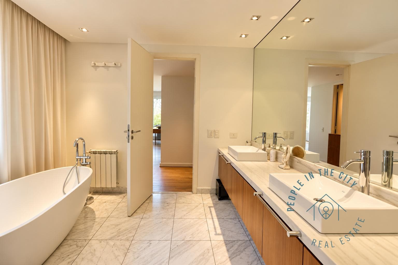 Baño moderno con bañera exenta y doble bacha sobre mesada de mármol.