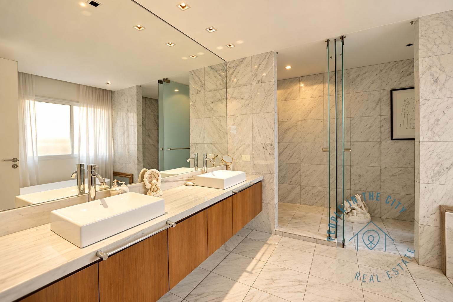 Baño con ducha de mampara de vidrio y doble lavatorio con mesada de mármol.