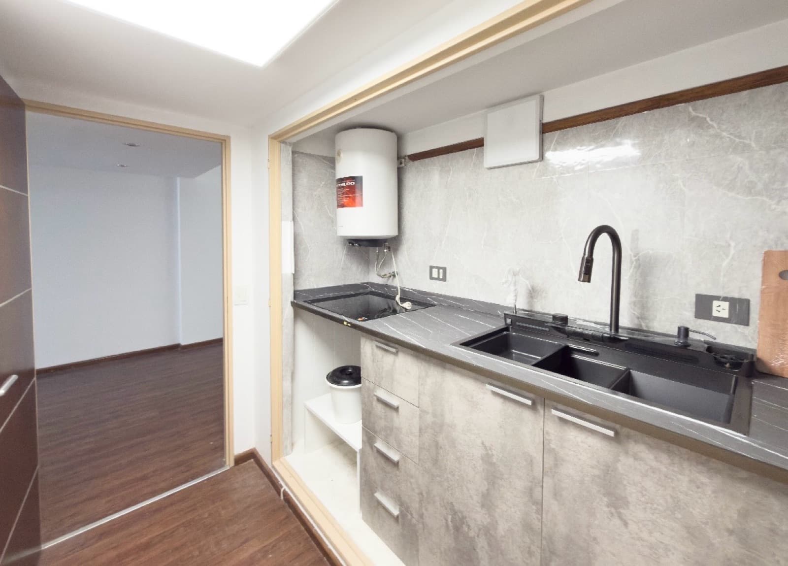 Cocina con mesada, bacha doble, grifo negro, termotanque y azulejos grises.