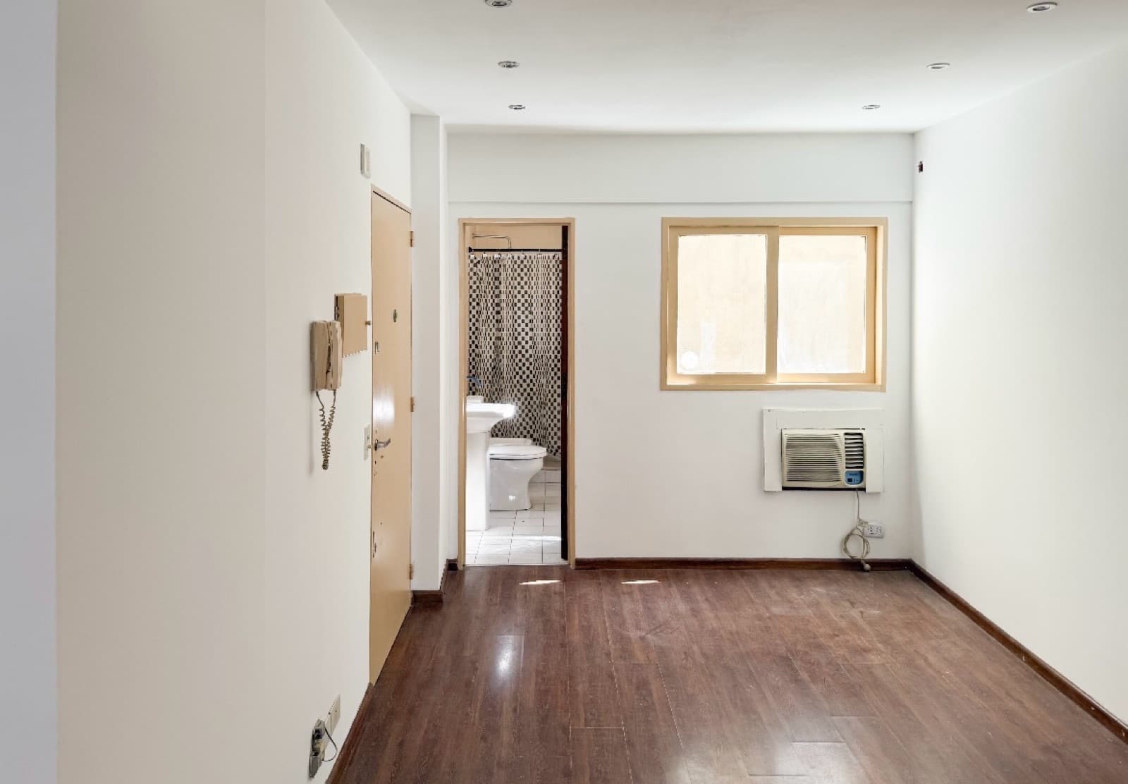 Pasillo con puerta de entrada, intercomunicador, baño al fondo y ventana.