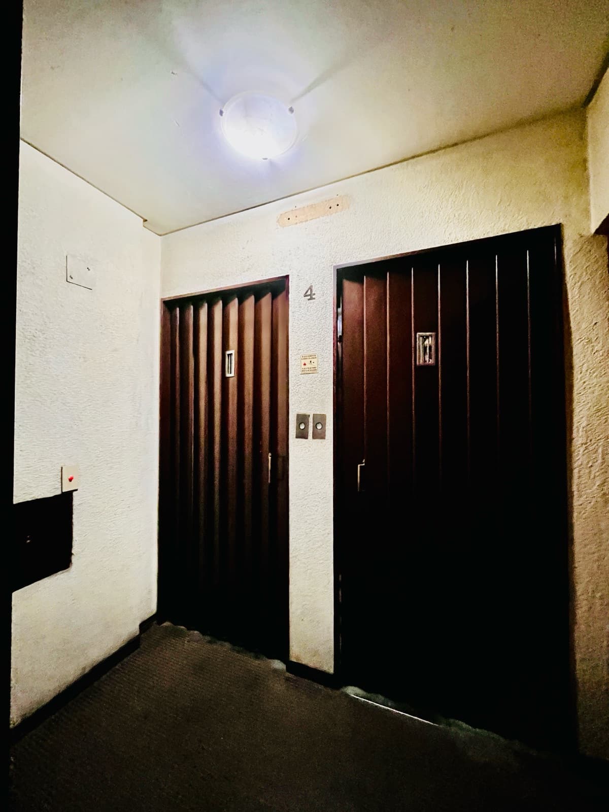 Palier del edificio con dos puertas de ascensor y paredes texturizadas.