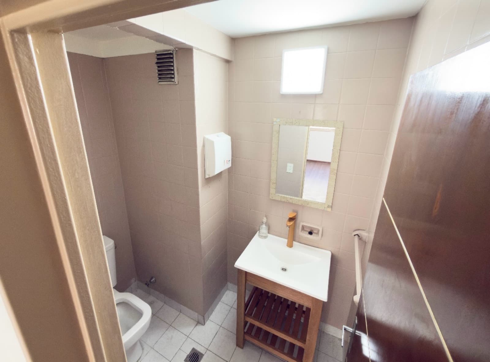Toilette con lavatorio de madera, inodoro, espejo y toallero.