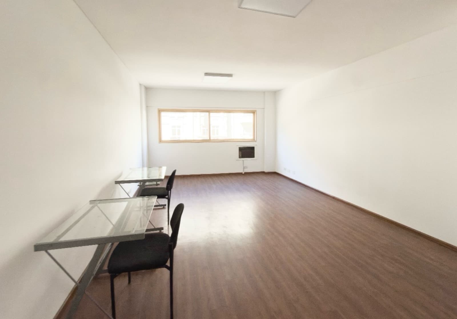 Amplio living vacío con algunas mesas y sillas, ventana grande.