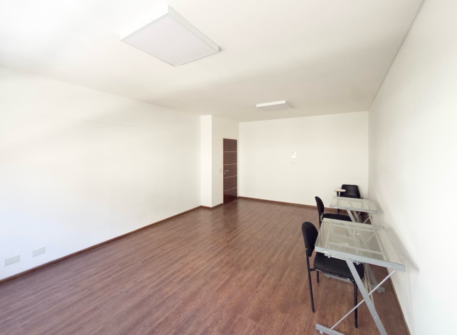 Amplio living vacío con algunas mesas y sillas, piso de madera.