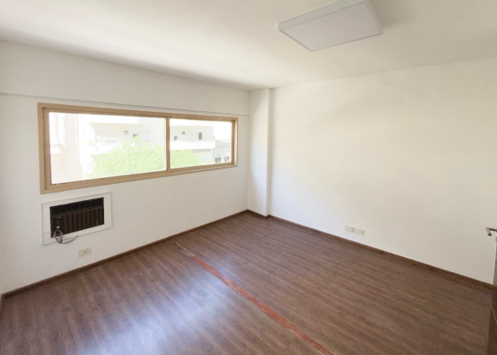Dormitorio vacío con ventana y aire acondicionado en la pared.