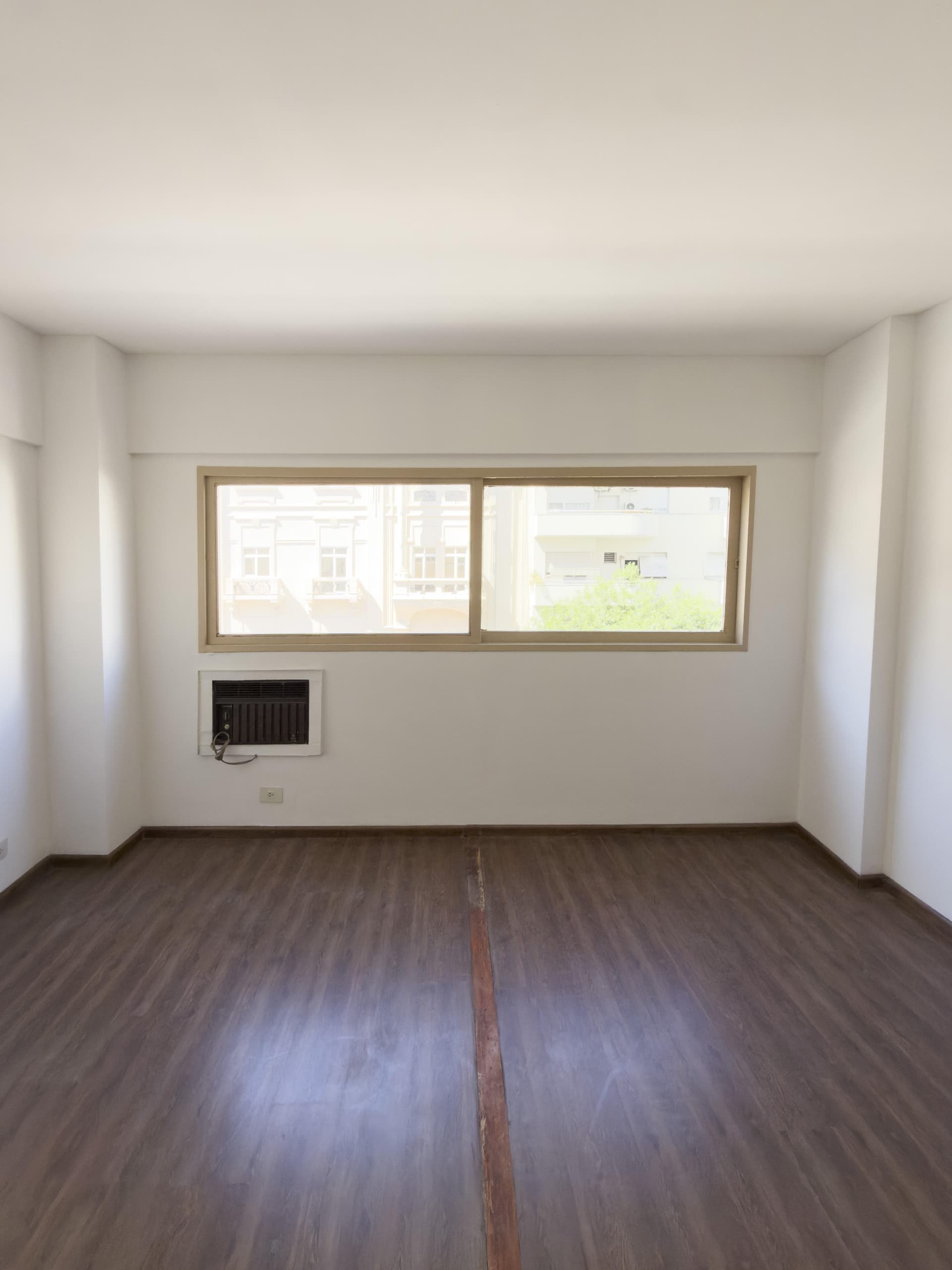 Dormitorio vacío con grandes ventanas y aire acondicionado en la pared.