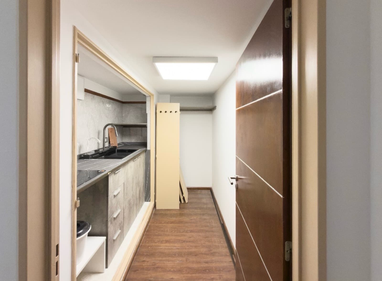 Cocina con mesada, bacha y termotanque, vista desde un pasillo.