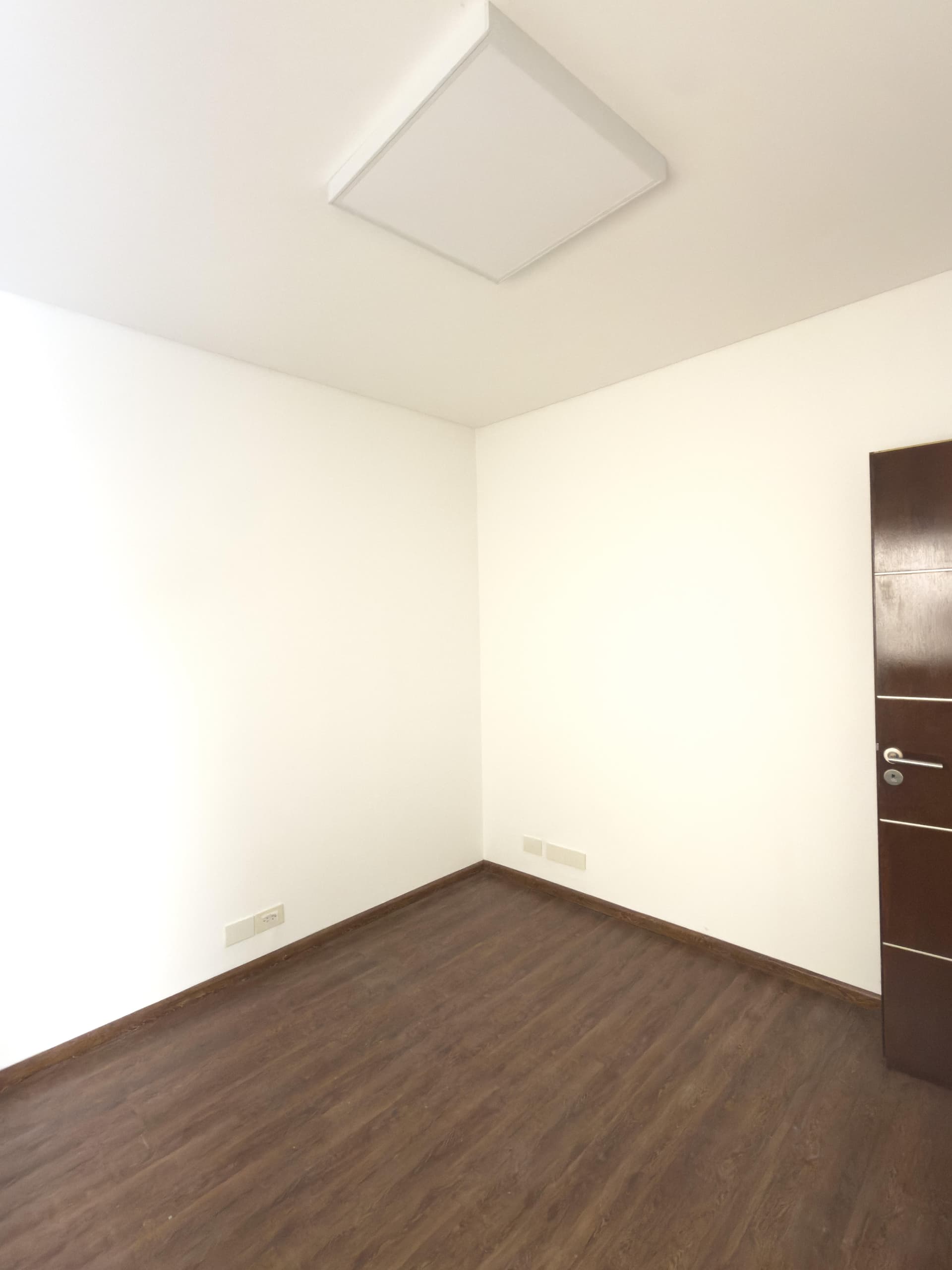 Dormitorio vacío con puerta de madera y piso laminado oscuro.