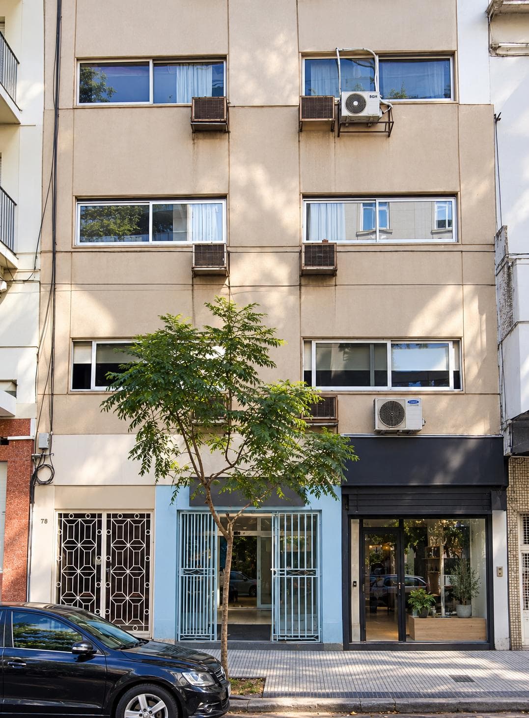 Fachada de un edificio con ventanas, aires acondicionados y un árbol en la calle.