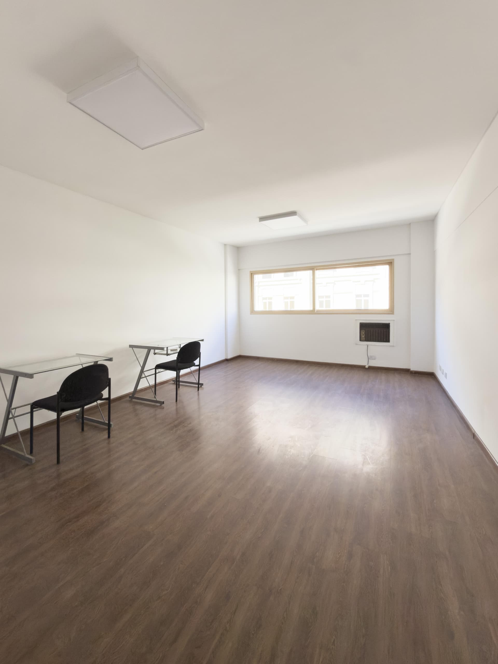 Amplio living vacío con algunas mesas y sillas, ventana grande.