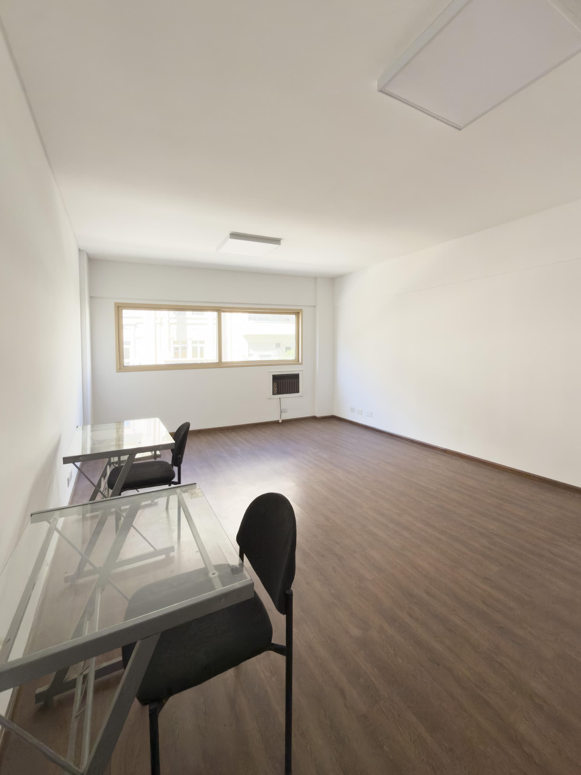 Amplio living vacío con algunas mesas y sillas, ventana grande.