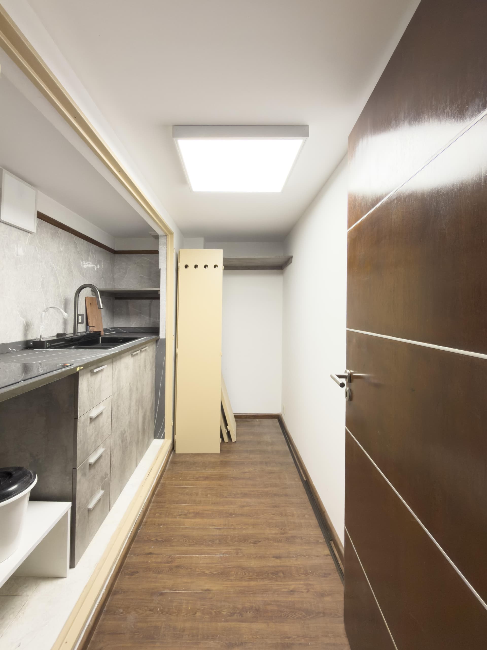Cocina con mesada, bacha y termotanque, vista desde un pasillo.