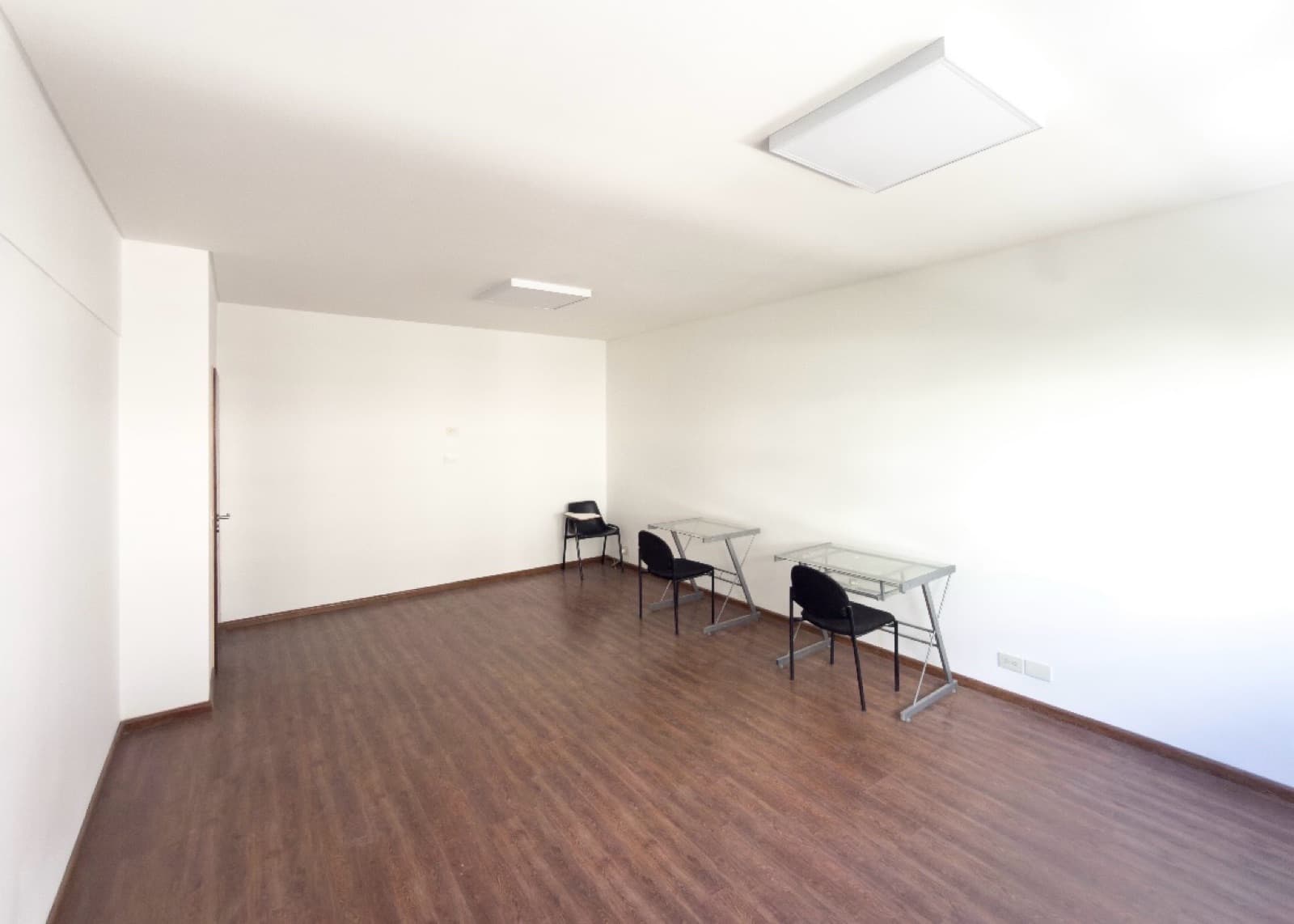Amplio living vacío con algunas mesas y sillas, piso de madera.
