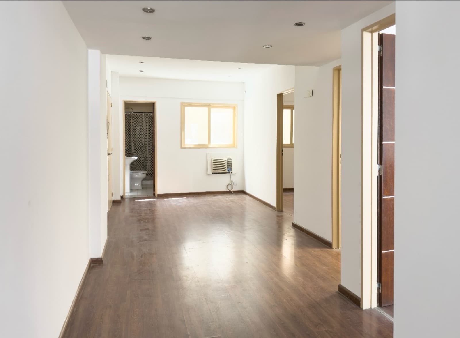 Pasillo largo con vista hacia un baño y una ventana con aire acondicionado.