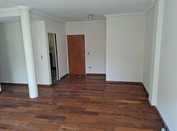 Living con piso de madera, puerta de entrada y acceso a otros ambientes.