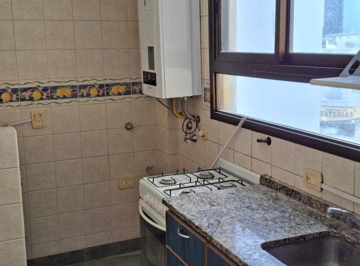 Cocina con anafe, bacha, termotanque, mesada de granito y ventana exterior.