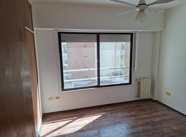 Dormitorio vacío con piso de madera, placard de madera y ventilador de techo.