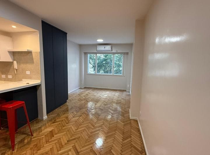 Living con piso de madera, mueble oscuro y ventana con aire acondicionado.
