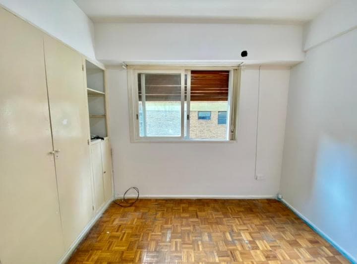 Dormitorio vacío con placard empotrado, ventana con persiana y piso de parquet.