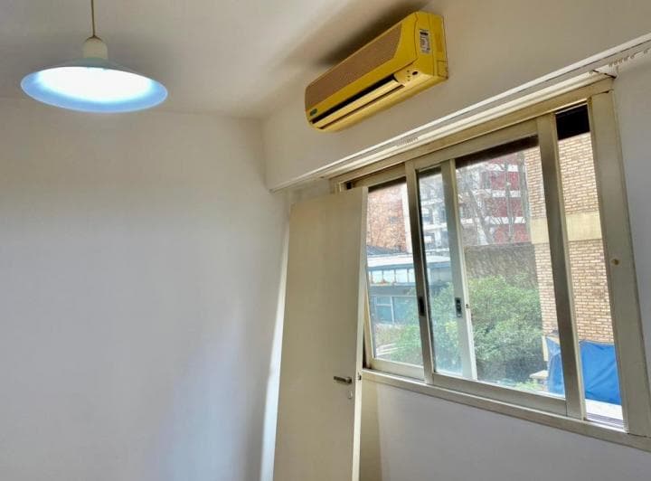 Dormitorio con ventana, aire acondicionado en la pared y puerta blanca.