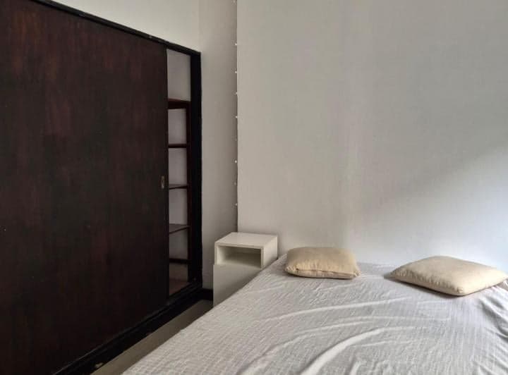 Dormitorio con cama individual, placard de madera oscuro y mesita de luz blanca.