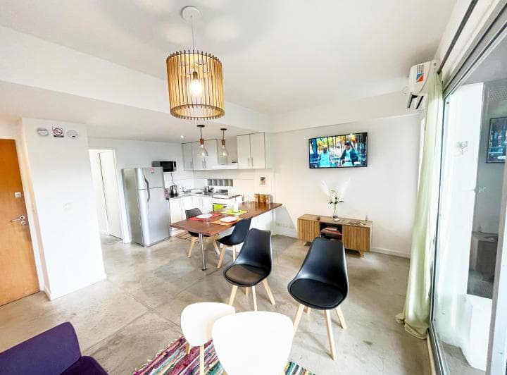 Living comedor con cocina integrada, sillón violeta y balcón al fondo